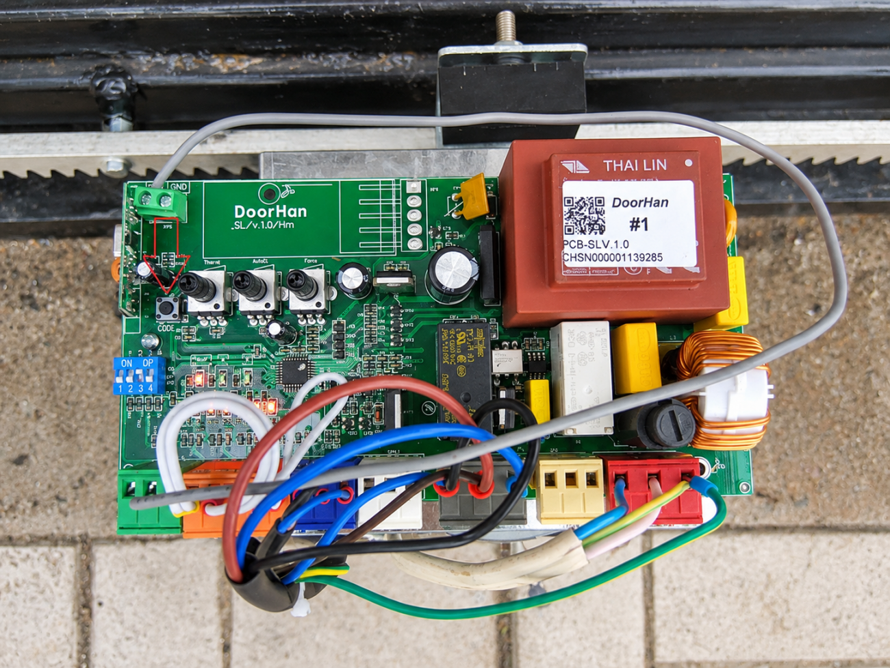 Плата управления DoorHan PCB-SL в приводе откатных ворот Плата управления DoorHan PCB-SL, установленная в приводе откатных ворот. На фотографии видны трансформатор, клеммные колодки, элементы настройки платы и подключённая силовая и управляющая проводка